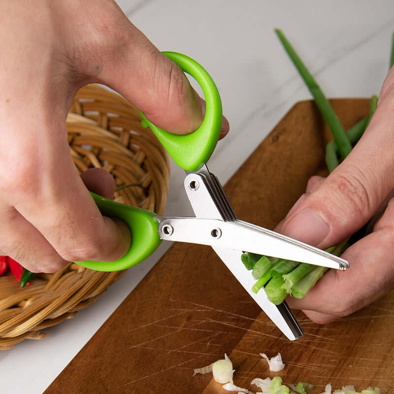 Multi-blade herb scissors with green handles cutting fresh green onions on a wooden board