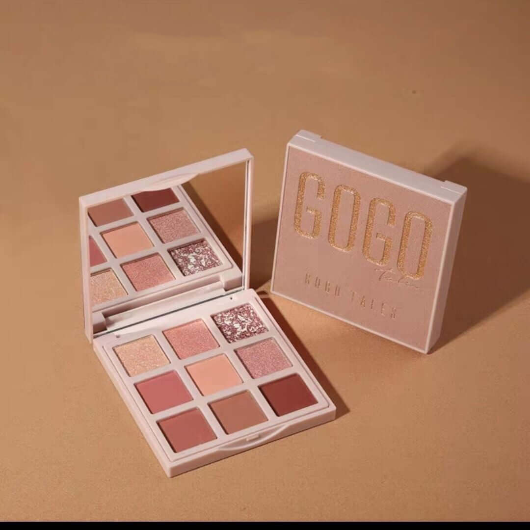 Pink and gold eyeshadow palette with mirror, featuring matte and glitter shades on beige background.
