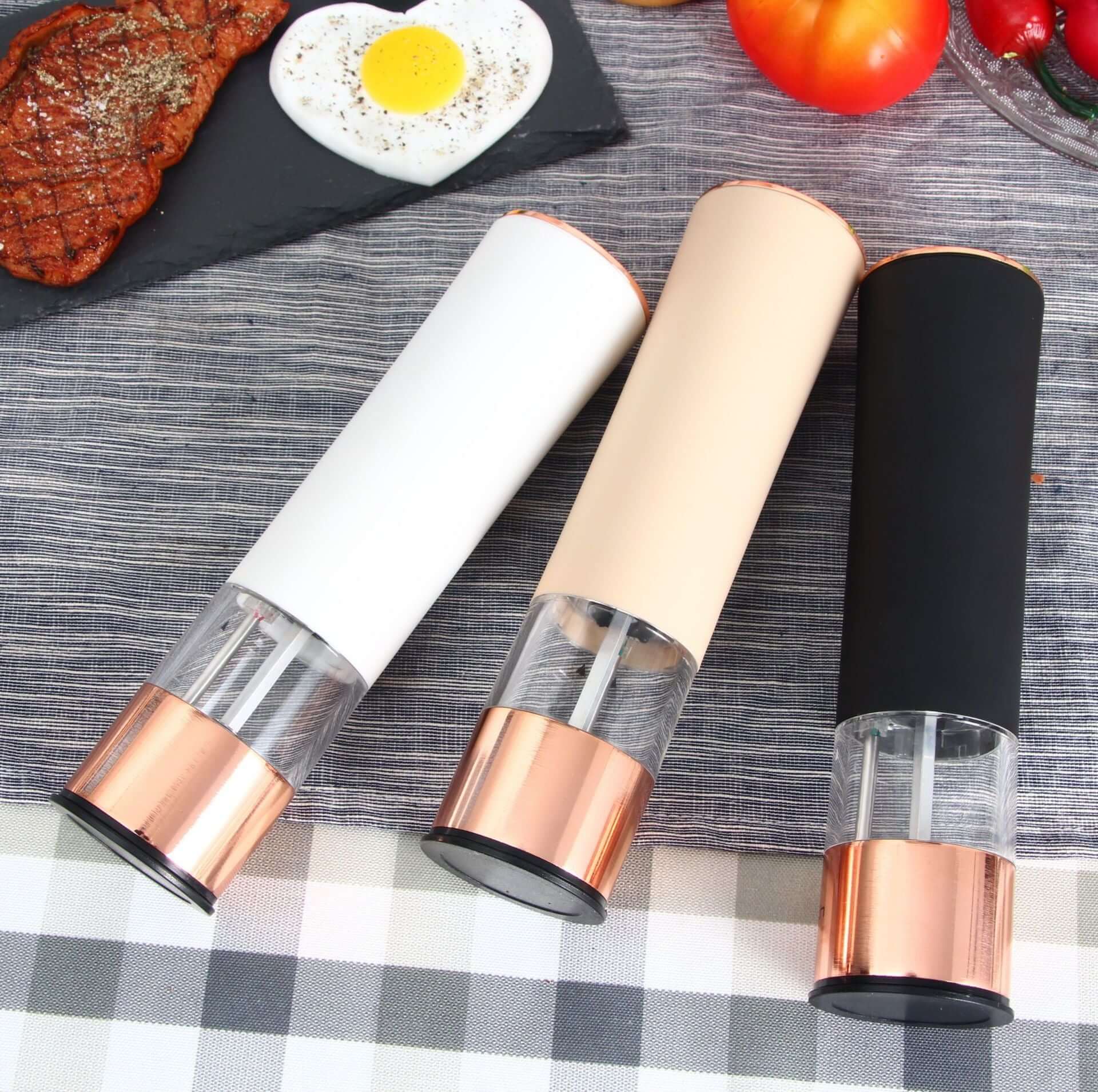Set of three electric pepper grinders in white, beige, and black on a kitchen table