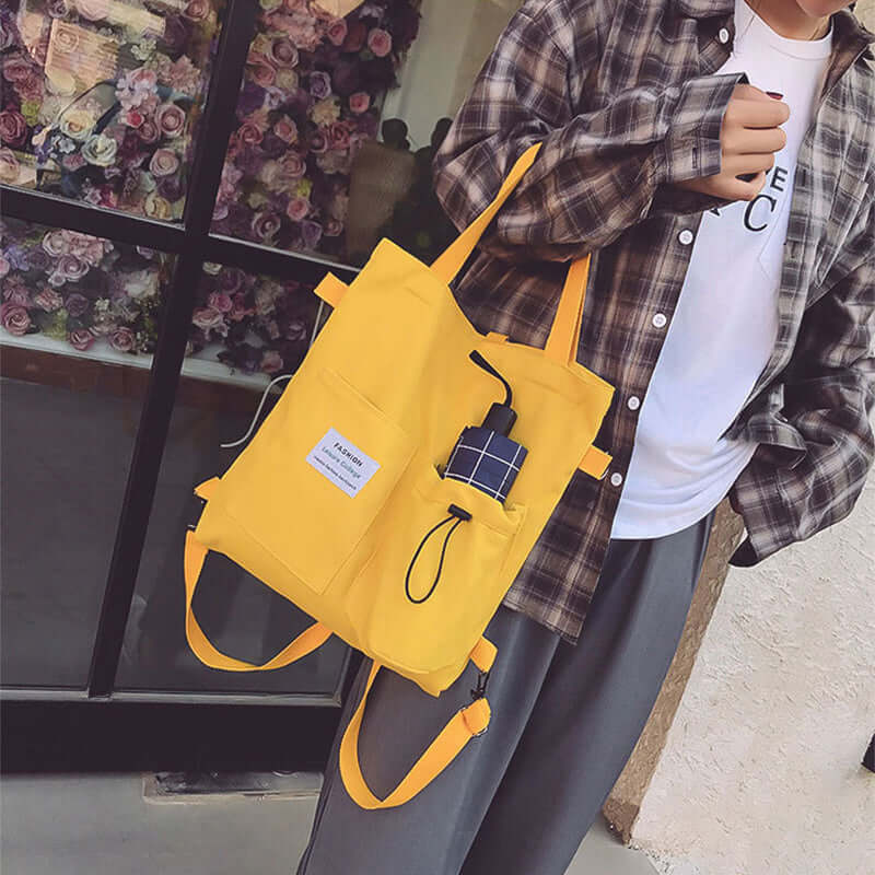 Person carrying a bright yellow tote bag with pockets, dressed in casual clothing