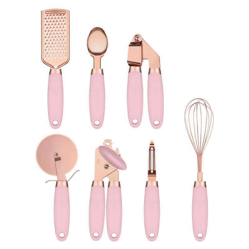 Pink and rose gold kitchen utensil set with grater, spoon, garlic press, whisk, pizza cutter, can opener, and peeler.