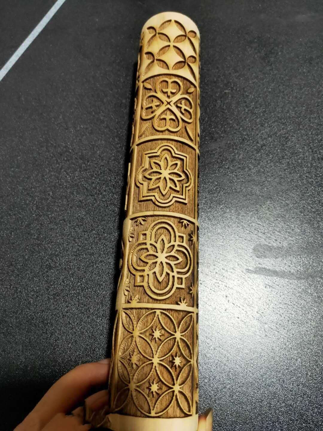 Wooden embossed rolling pin with floral and geometric patterns on a dark surface