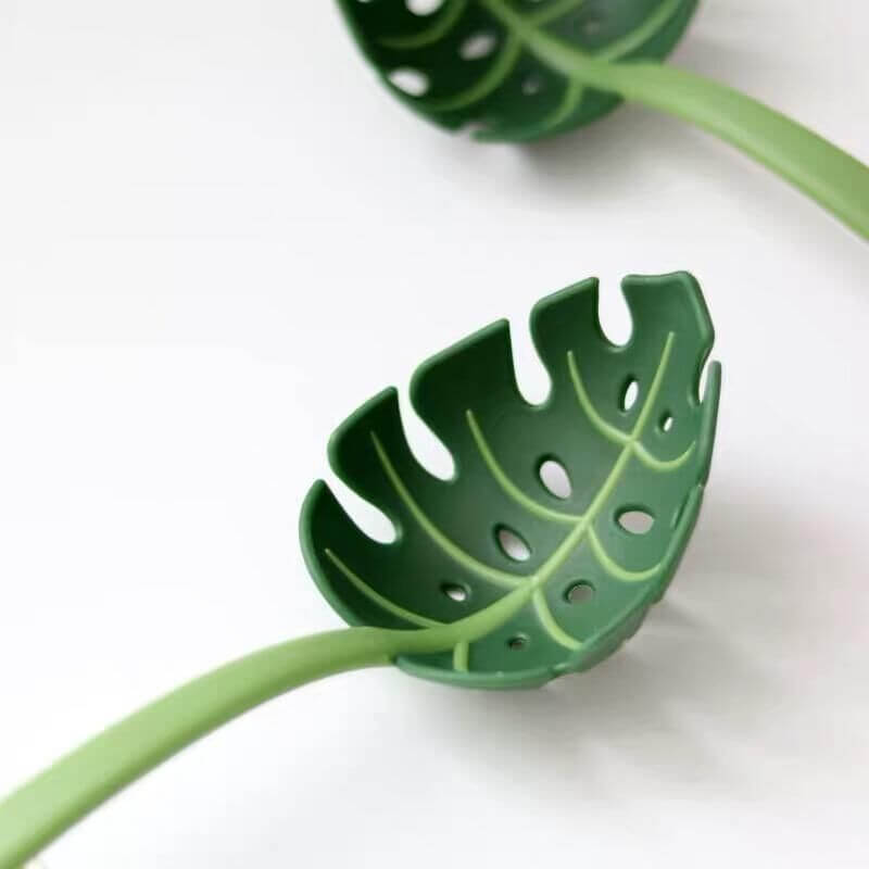 Green leaf-shaped kitchen colander spoon utensil with holes, isolated on white background