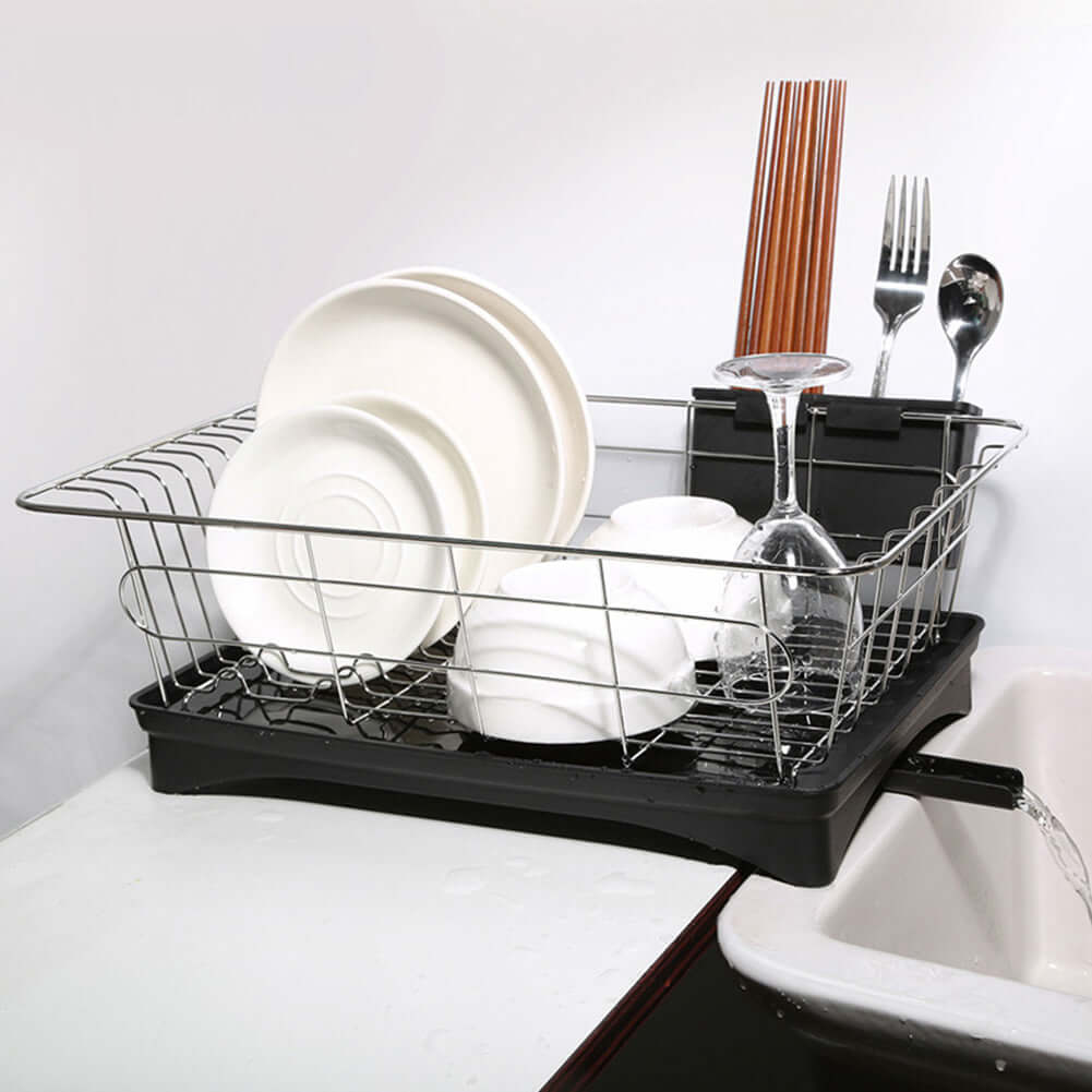 Stainless steel dish drying rack with plates, bowls, utensils, and wine glass by sink