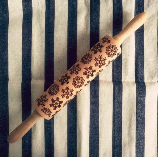 Wooden rolling pin with snowflake pattern on striped kitchen towel