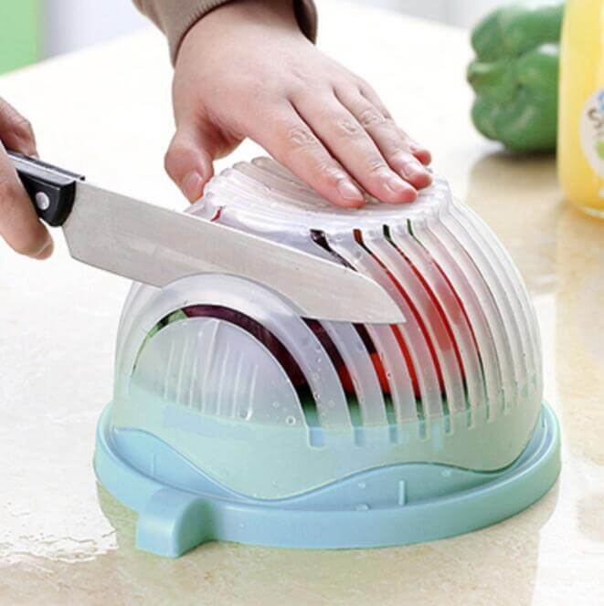 Hand using kitchen salad cutter bowl to slice vegetables with knife on countertop