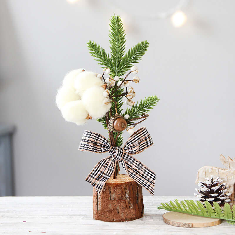 Mini artificial pine tree ornament with cotton flower, berries, and plaid bow on wood base, holiday decor.