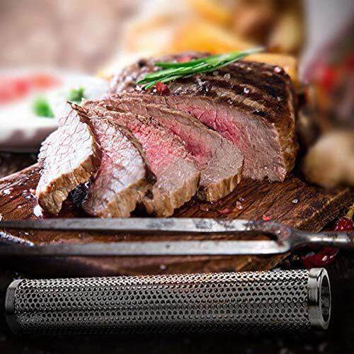 Grilled beef steak sliced on cutting board with meat fork and stainless steel smoker tube.