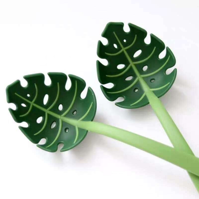 Leaf-shaped green kitchen utensils with hole design on a white background
