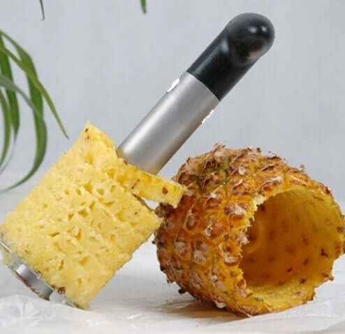 Stainless steel pineapple corer with black handle and peeled pineapple next to hollowed shell