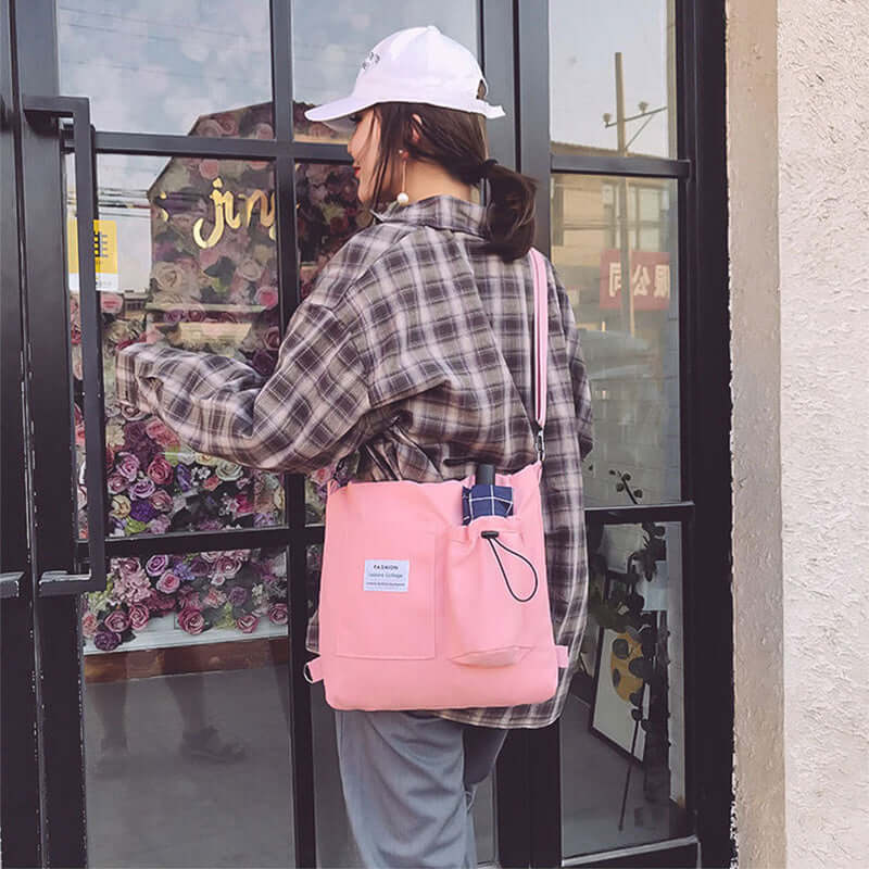 Woman in plaid shirt and white cap carrying pink tote bag outside glass door with flower display