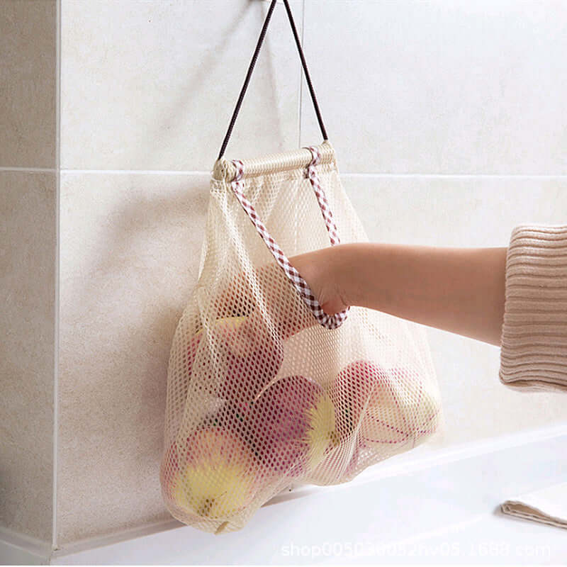 Hand taking apples from hanging mesh kitchen storage bag on tiled wall