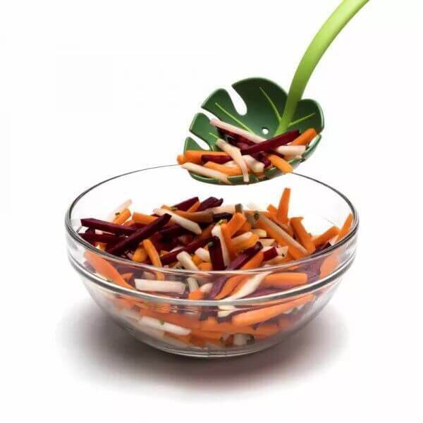 Glass bowl of vegetable sticks with green leaf-shaped kitchen serving spoon