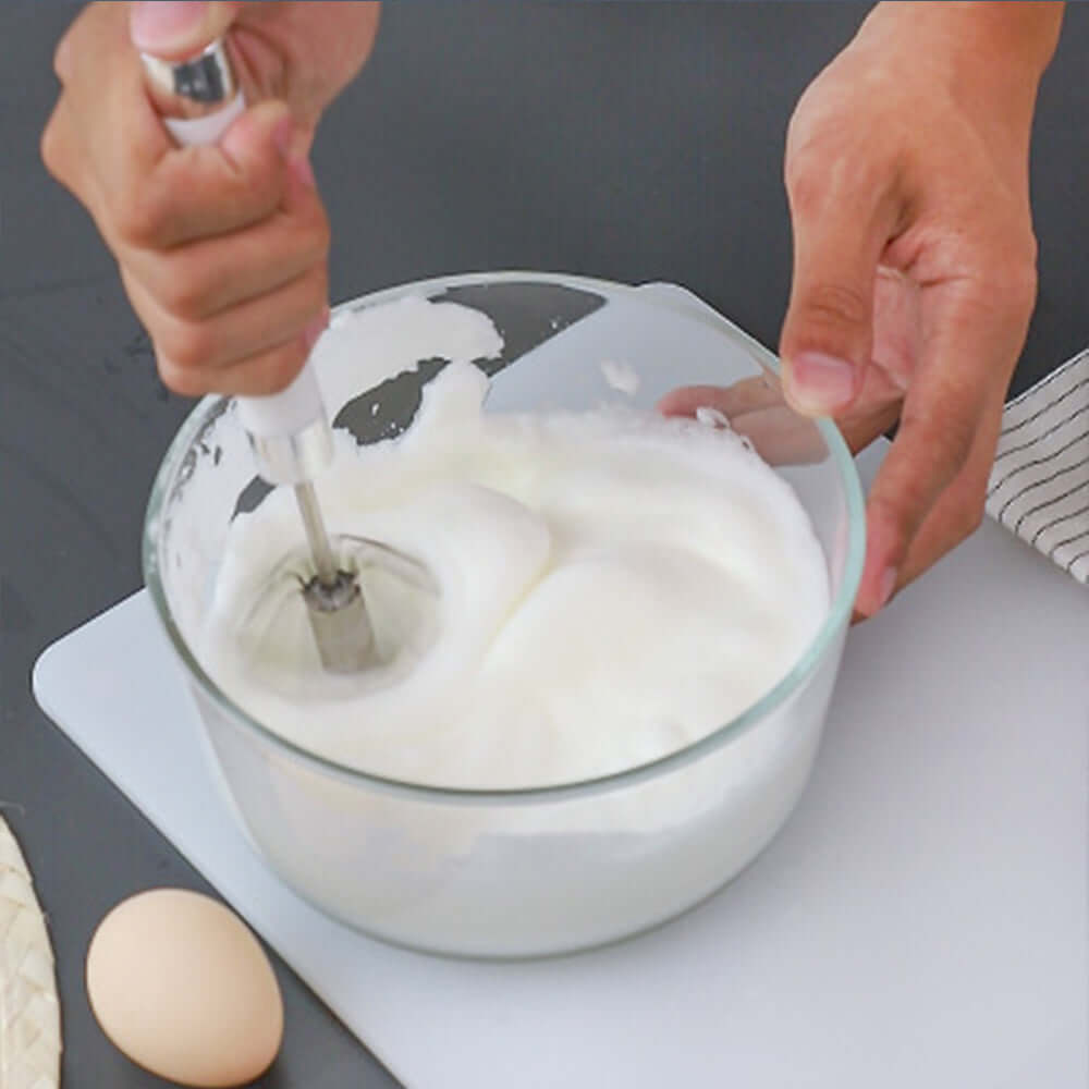 Hand whisking egg whites in glass bowl with kitchen utensil on counter