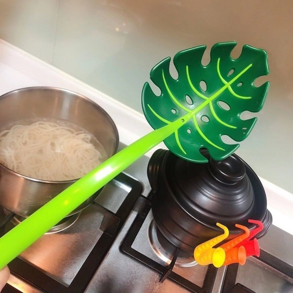 Leaf-shaped pasta strainer utensil over stovetop with pot and boiling noodles, kitchen accessories