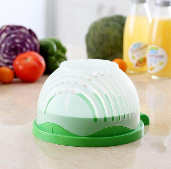 Salad cutter bowl kitchen accessory on counter with vegetables and juice bottles in background
