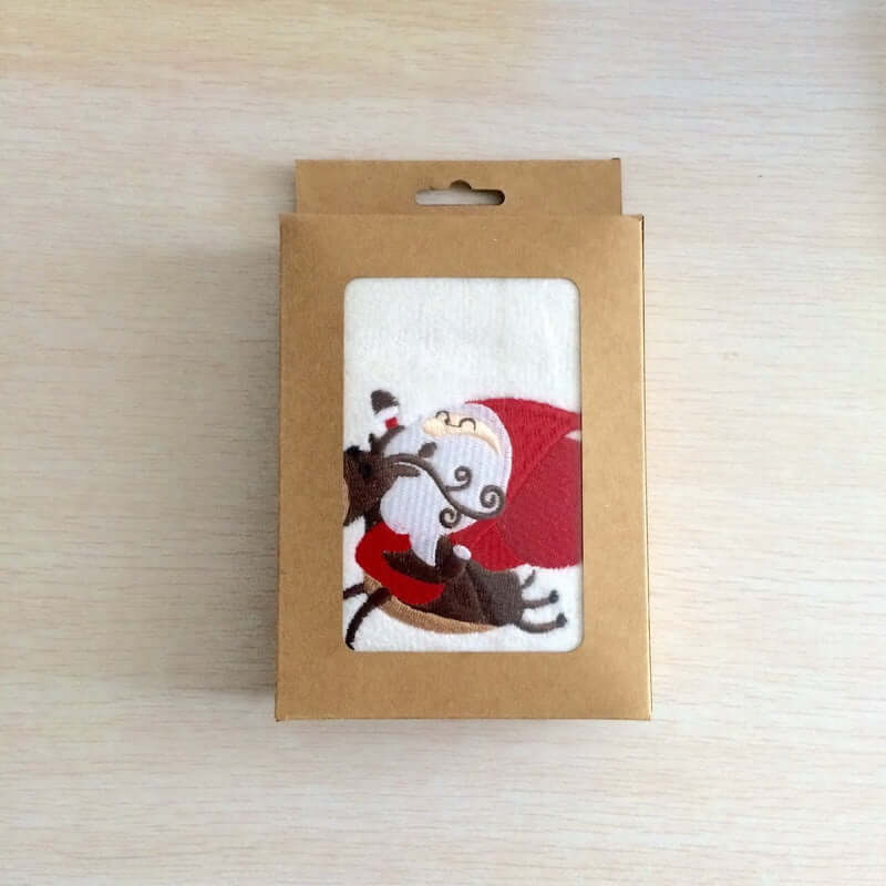Christmas kitchen towel in box with Santa and reindeer design on light wood surface