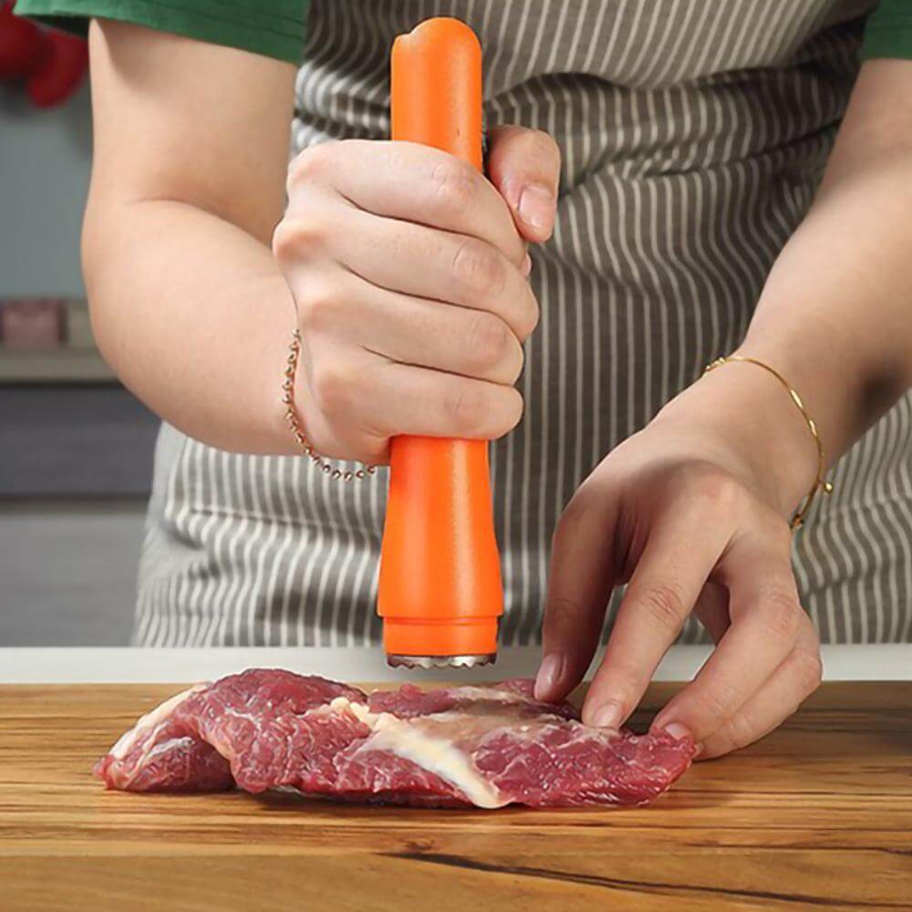 Person using orange meat tenderizer tool on raw steak on wooden cutting board