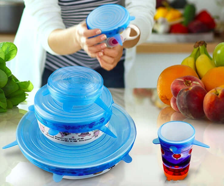 Reusable silicone stretch lids covering bowls and cups on a kitchen counter with fresh fruit.