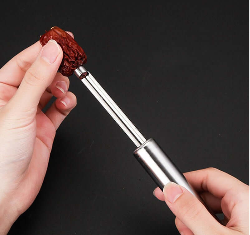 Hand using stainless steel fruit pitter tool on a date, kitchen utensil on black background