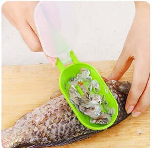 Hand using green fish scaler tool to remove scales from fish on wooden cutting board