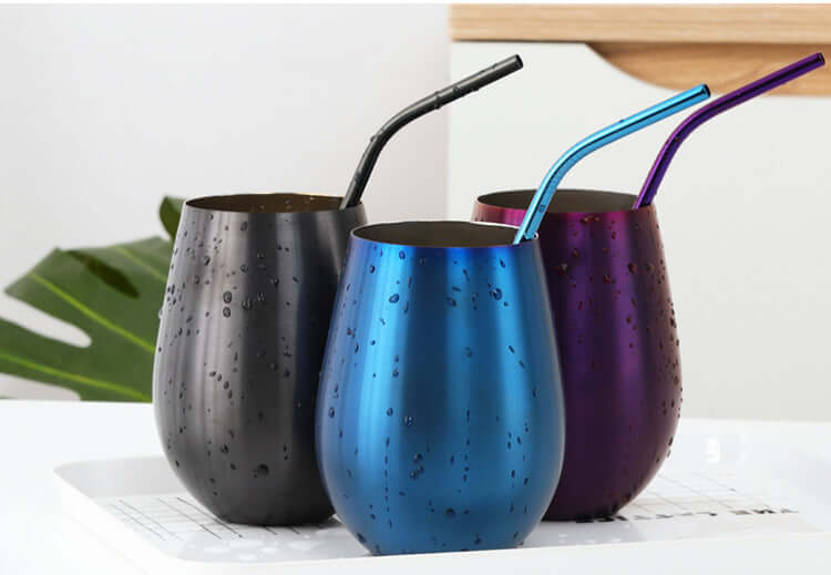 Three stainless steel tumblers with metal straws in black, blue, and purple on a kitchen counter