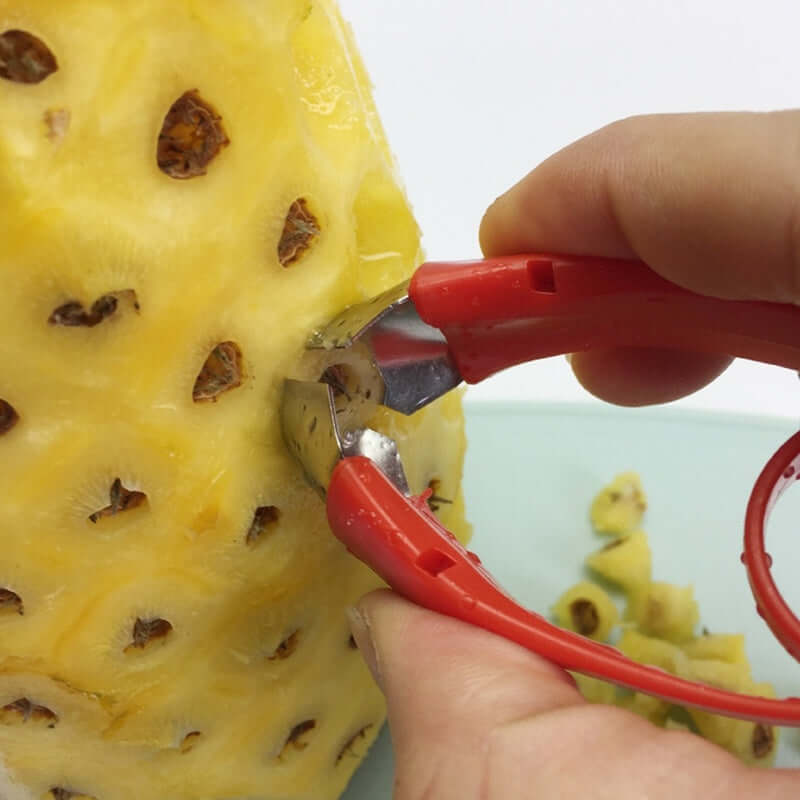 Hand using red handle kitchen tool to remove pineapple eyes from peeled pineapple