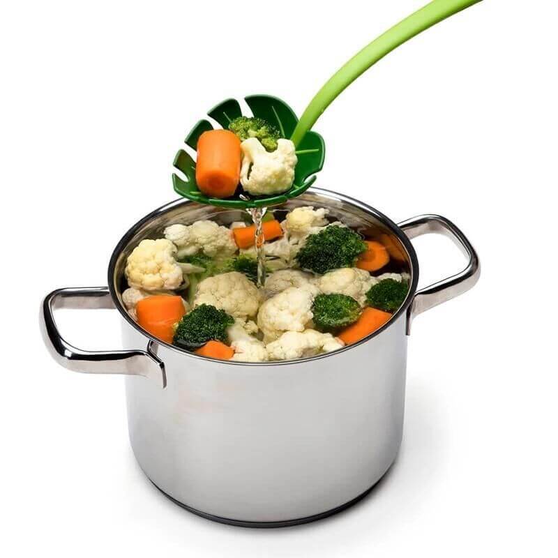 Green slotted kitchen ladle draining vegetables from a stainless steel pot
