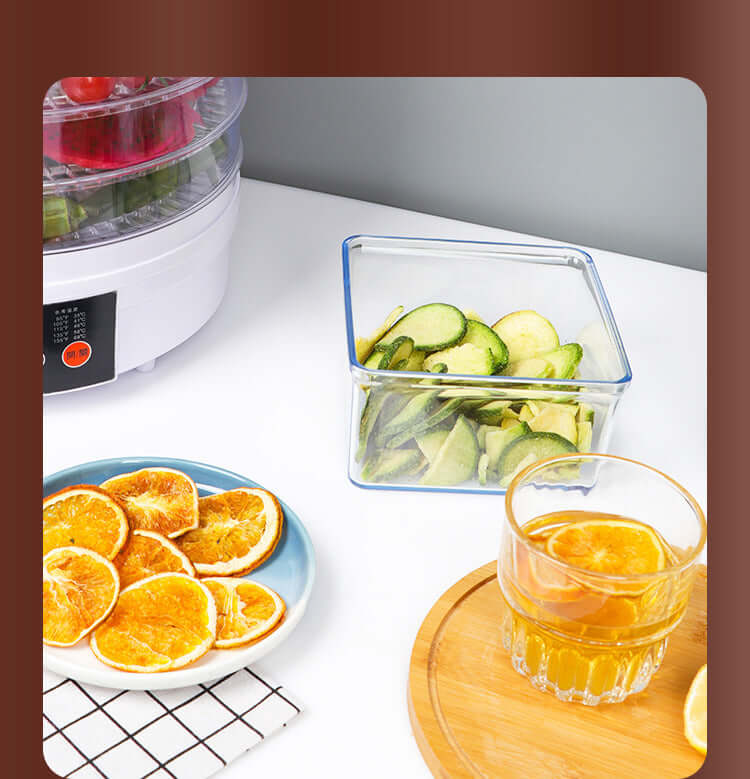 Dehydrator machine with dried orange slices, cucumber chips in container, and juice on kitchen counter