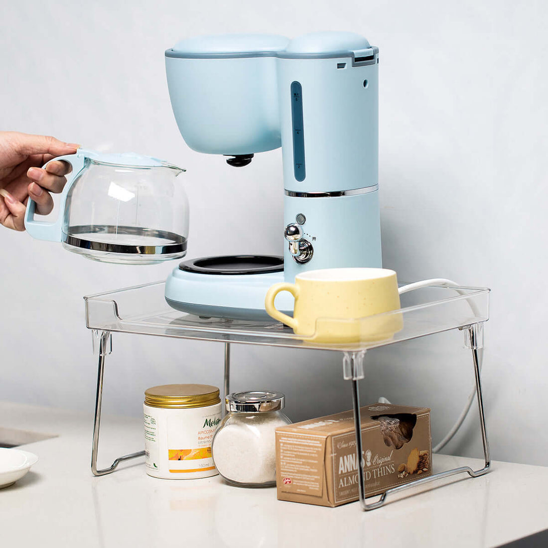 Blue coffee maker with glass carafe, yellow mug, and kitchen storage shelf on counter