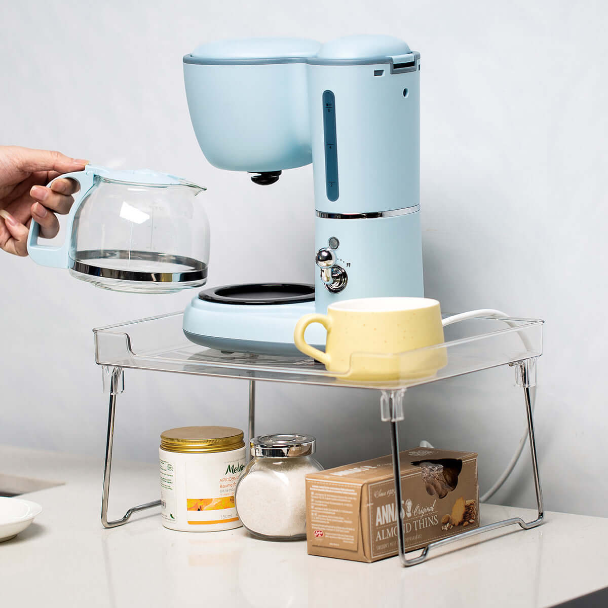 Blue coffee maker with glass carafe, yellow mug, and kitchen storage shelf on counter
