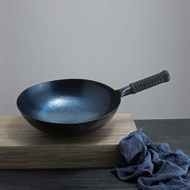 Black nonstick wok with textured surface and rubber handle on wooden cutting board