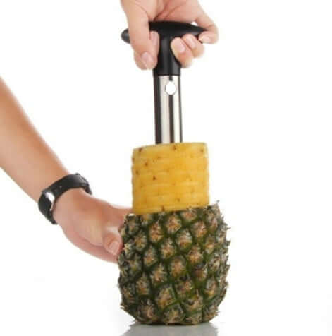 Hand using stainless steel pineapple corer and slicer with fresh pineapple on white background