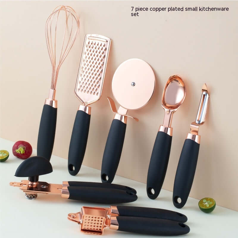 Copper plated kitchen utensil set with black handles including whisk, grater, pizza cutter, peeler.
