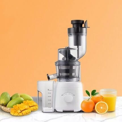 Electric juicer machine with fresh mangoes, oranges, and juice on a marble kitchen counter