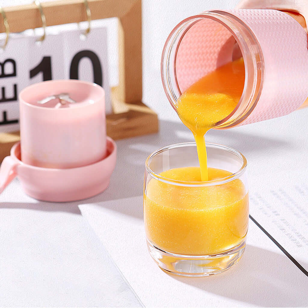 Portable pink blender pouring fresh orange smoothie into a glass on a kitchen table