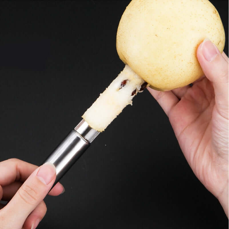Stainless steel apple corer removing core from fresh apple on black background