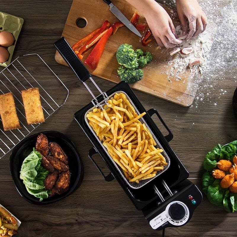 Electric deep fryer with French fries, fresh vegetables, and fried foods on kitchen table