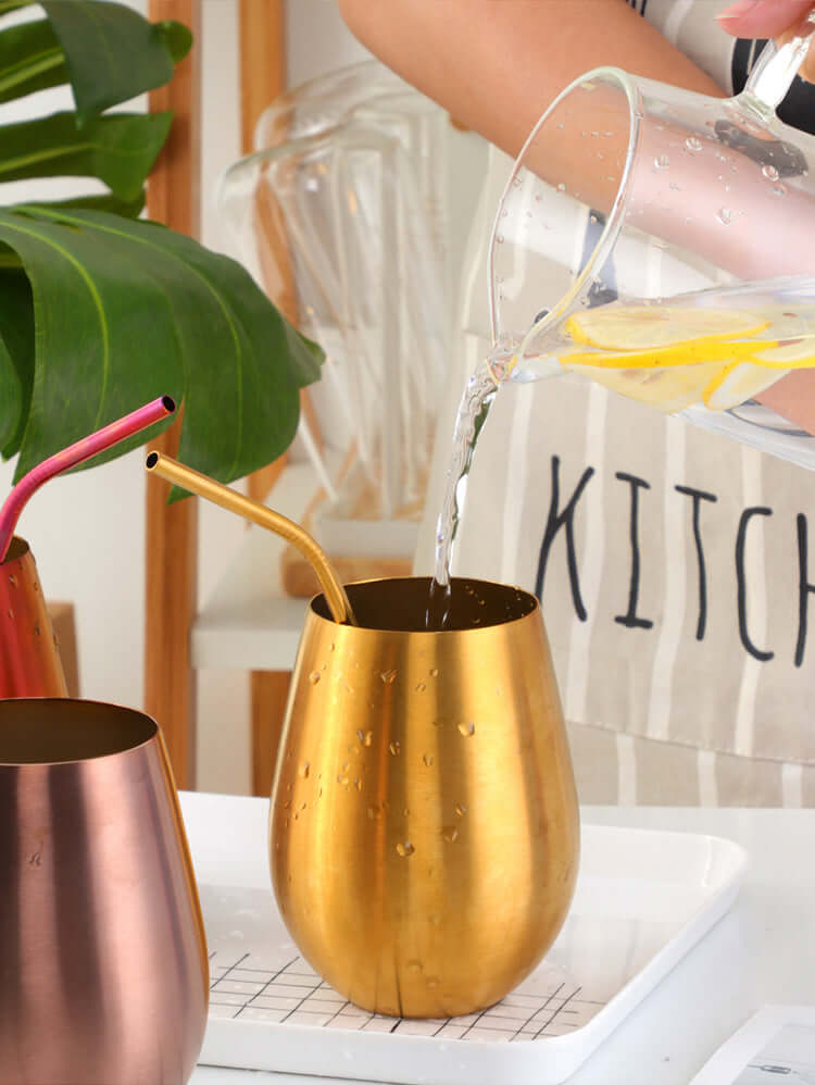 Pouring infused water into a gold stainless steel tumbler with metal straw in a kitchen.