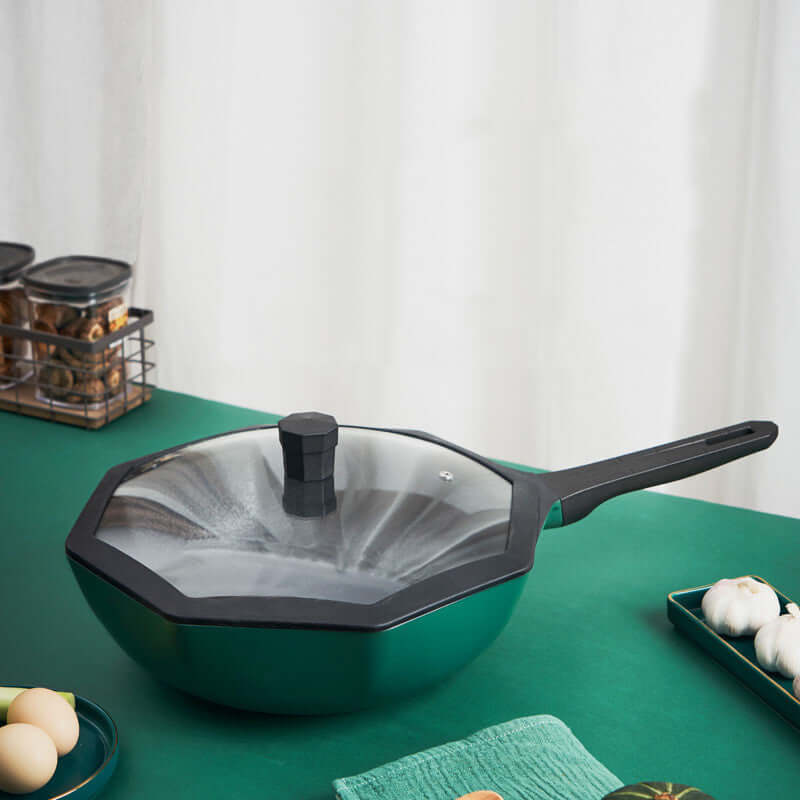 Nonstick deep frying pan with glass lid and black handle on a green kitchen countertop