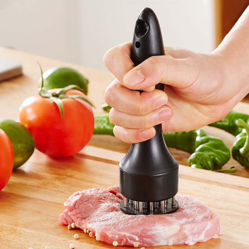Hand using a meat tenderizer tool on raw pork steak on kitchen cutting board with vegetables