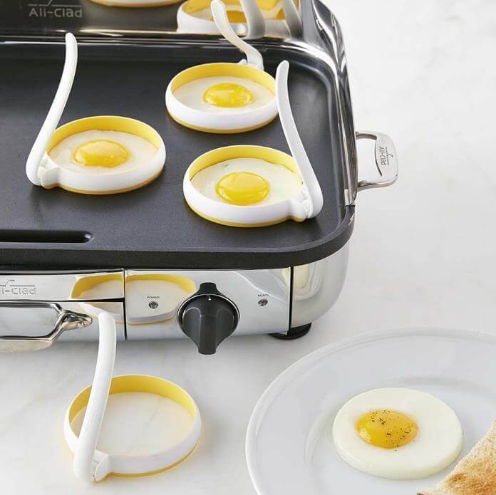 Eggs cooking on a griddle using round egg molds for uniform shape, breakfast kitchen accessory.