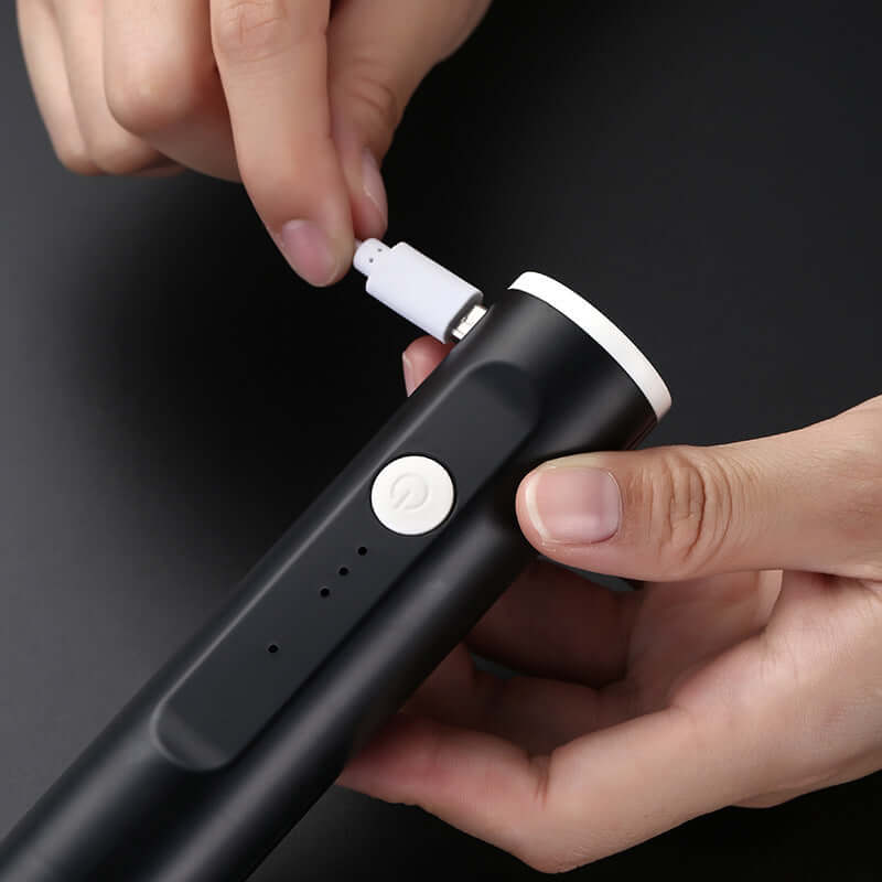 Hand charging a black electric kitchen gadget with a USB cable on dark background