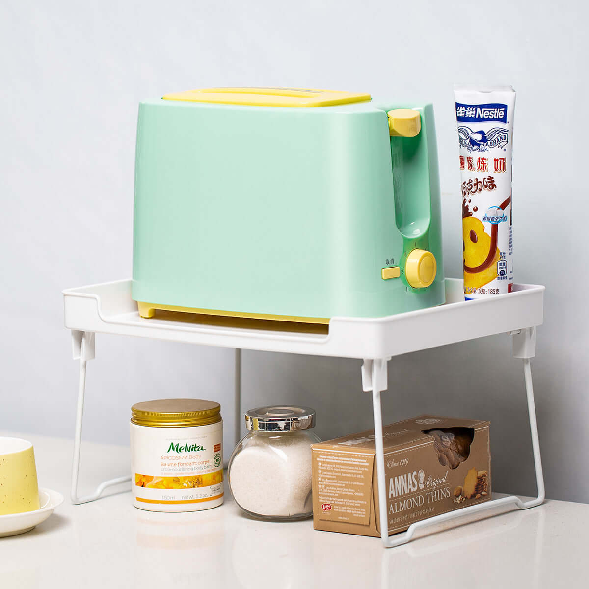 Mint green toaster with yellow accents on white kitchen shelf, surrounded by snacks and condiments.