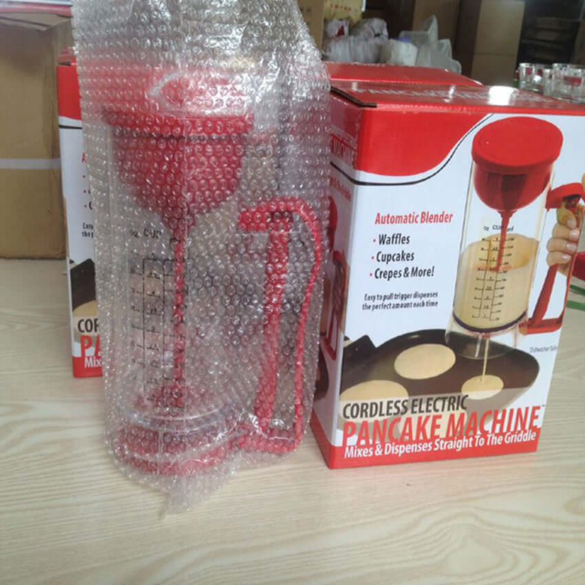 Cordless electric pancake machine with red dispenser, packaged beside product box on wooden table