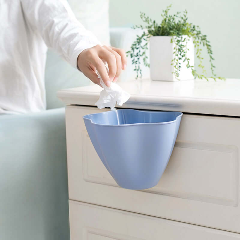 Blue plastic hanging trash bin attached to cabinet, hand dropping tissue waste