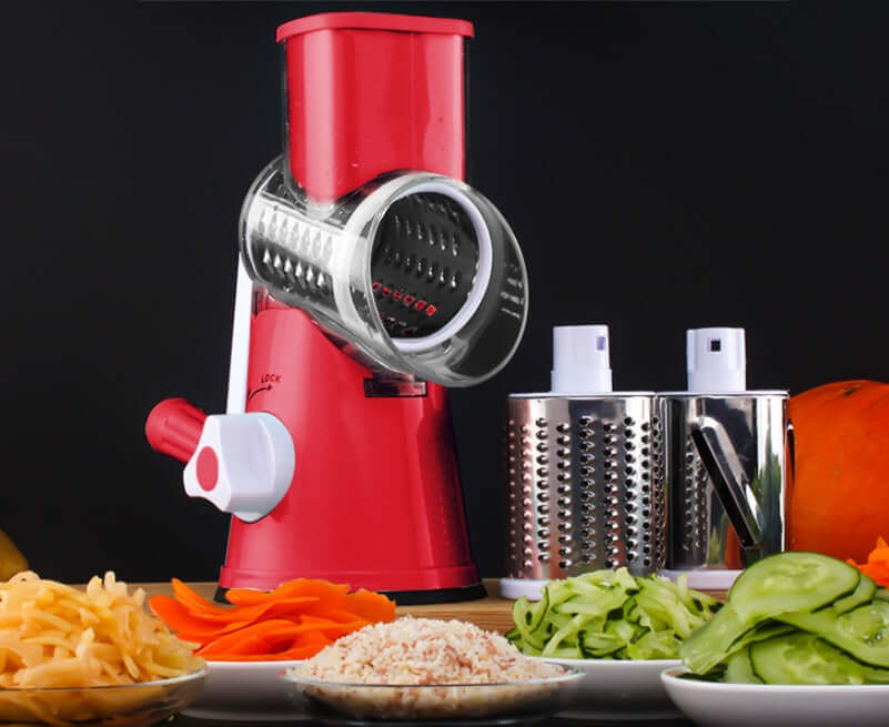 Red rotary vegetable slicer with interchangeable grater drums, surrounded by sliced vegetables