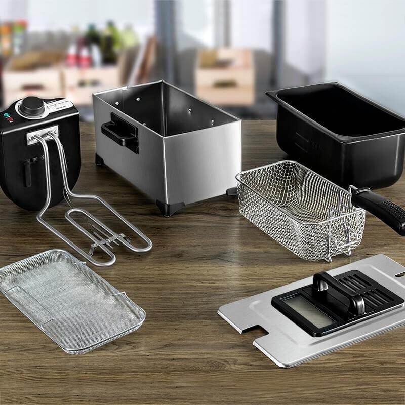 Stainless steel electric deep fryer with removable basket and parts on a wooden kitchen table