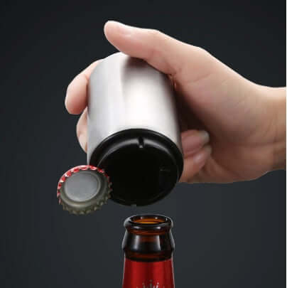 Hand using stainless steel bottle opener to remove cap from glass bottle
