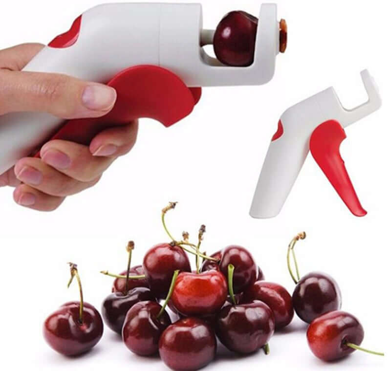 Handheld cherry pitter kitchen tool with red handle beside fresh cherries